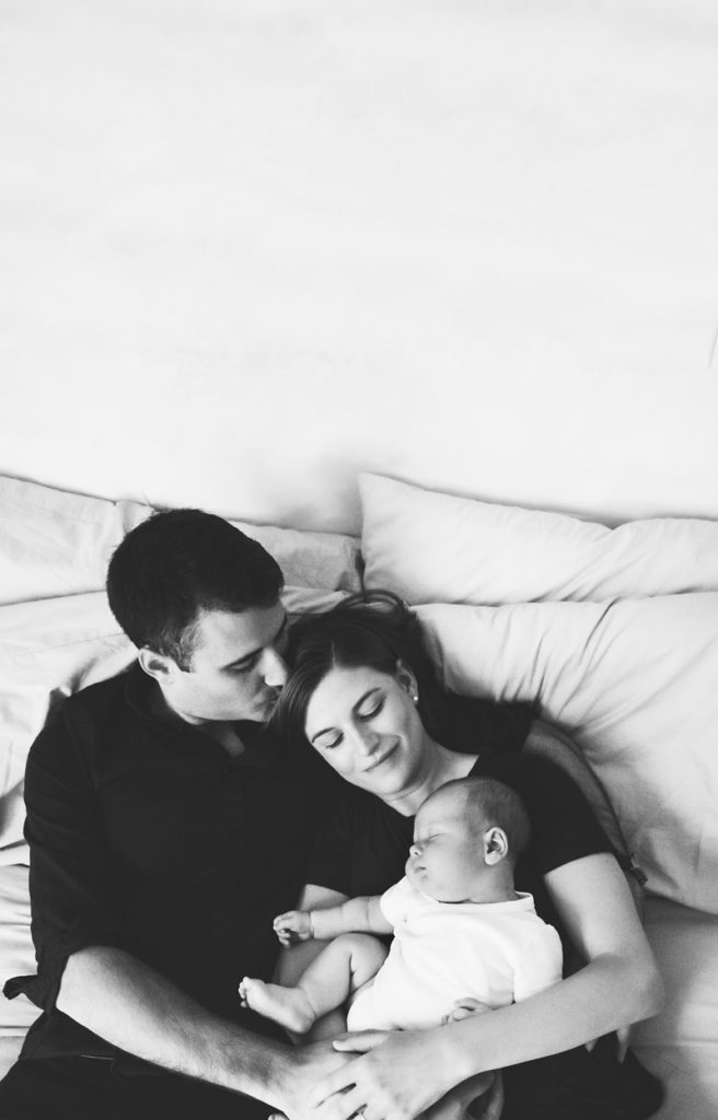 photograph of family, man and woman snuggle on couch holding newborn